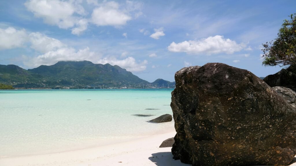 Top 10 des plus belles îles paradisiaques 🌴 A stunning view of a tropical beach with clear waters, blue skies, and distant mountains.